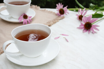Herbal tea in a white cup, fresh and dried flowers of Echinacea, napkin on a marble background. Side view. Space for text. 