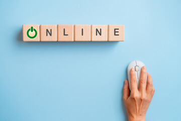 Online  and symbol on wooden cube block with hand using computer mouse on blue background for...
