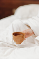 Person sitting in bed with a cup of tea in their hand, covered with a white sheet