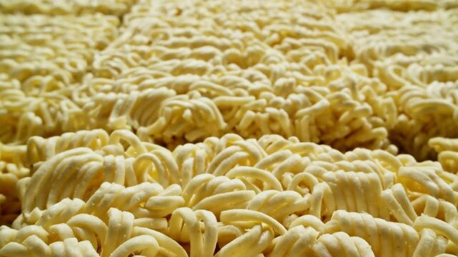 Instant noodles. Row of dehydrated ramen noodles, ready to be cooked. Close-up of raw dried noodles. Uncooked noodles texture. Junk food concept. Factory of production. Dolly shot. 4K, UHD