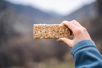 Close up of female hand holding grain cereal bar snack on the hike, dessert, muesli, healthy food,...