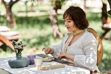 A young woman enjoys a summer brunch outdoors, dressed in a white dress and a straw hat.