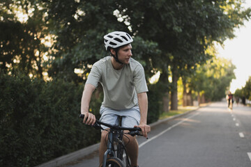 Obraz premium athlete man in a helmet rides a road bike down a paved path in a park, during the day