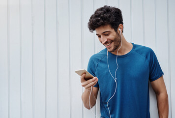 Earphones, exercise and man with smartphone, wall and happiness with motivational podcast. Wellness, healthy person and athlete with cellphone, social media and online for audio, fitness and workout