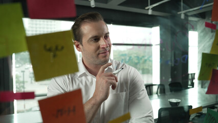 Smart businessman thinking about start up project in front of glass board. Smiling male project...