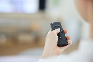 リビングにて動画配信サービスを楽しむ日本人女性の手元とリモコン