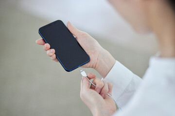 スマートフォンに充電器のコードを差し込む日本人女性の手元