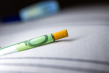 A cigarette butt is on a white surface next to a green bill
