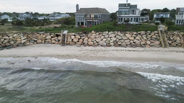 Solo girl walks along sandy shore on the Nantucket sound below oceanfront houses, aerial tracking