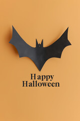 A paper cut out bat on an orange background with "Happy Halloween" lettering. Design for a card or poster for Halloween. Cute animal. Minimalism