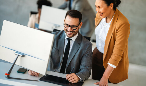 Senior business manager talking with experienced colleague while using computer in office.