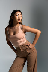 Fototapeta premium A woman in a pink tank top and brown pants poses confidently in a studio setting.