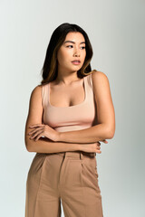 Obraz premium A beautiful Asian woman in a peach tank top and brown pants poses with her arms crossed.