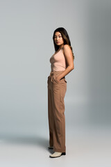 Fototapeta premium Woman in studio, confidently gazing, wearing pink tank top and brown pants.