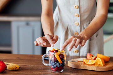 Close-up of a glass bowl with fruits and berries and a female hands.