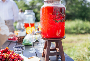 A wooden table with sweet berries and fruits, jars of freshly squeezed juice and empty glasses.
