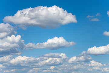 Fototapeta premium A photo of fluffy white clouds against a bright blue sky. The clouds appear to be cumulus, with some larger clouds in the middle of the frame.