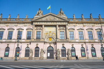 Fototapeta premium The German Historical Museums grand facade bathes in sunlight against a clear blue sky on Unter den Linden Street in Berlin, Germany