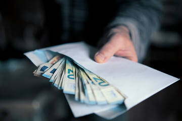 Man hand giving an envelope full of euros banknotes.
