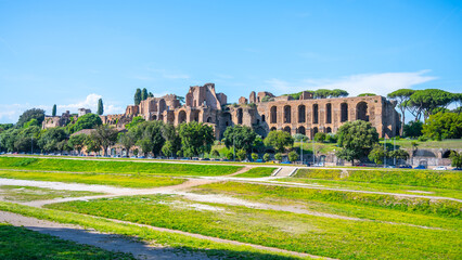 A view of the Domus Severiana ruins on Palatine Hill from Circus Maximus in Rome, Italy. The ancient Roman palace is visible in the distance, with a grassy area in the foreground.