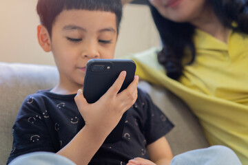 Fototapeta premium Close up cute little Asian boy with mom using smartphone, looking at screen