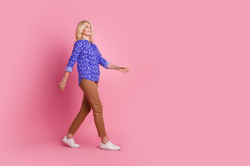 Full size profile photo of pretty aged lady walk empty space wear shirt isolated on pink color background