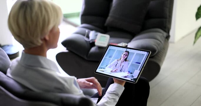 Blonde woman talks on video call with doctor via tablet complaining on pain in heart. Female patient at online consultation with specialist slow motion