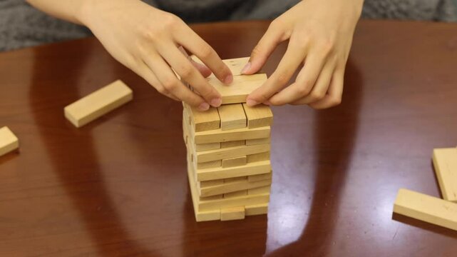 A person carefully removes a block from a tower of wooden blocks in a game of Jenga
