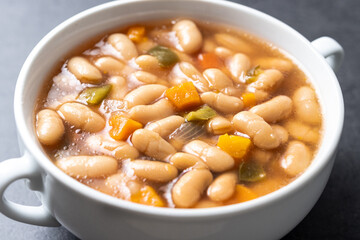 White beans soup with vegetables in white bowl on black stone. Close up