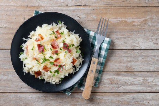 Slovak potato dumplings halusky with steamed sauerkraut and bacon on wooden table. Top view. Copy space