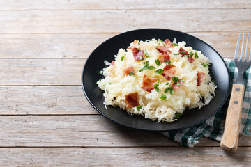 Slovak potato dumplings halusky with steamed sauerkraut and bacon on wooden table. Copy space