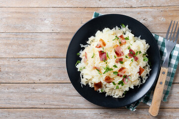 Slovak potato dumplings halusky with steamed sauerkraut and bacon on wooden table. Top view. Copy space