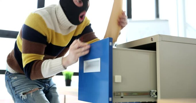 Clever thief with black mask on face unlocks safe with clip. Anonymous man opens drawer taking folder with valuable documents in office