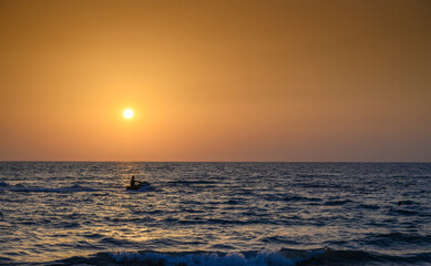 Calm sea with sunset sky and sun through the clouds over