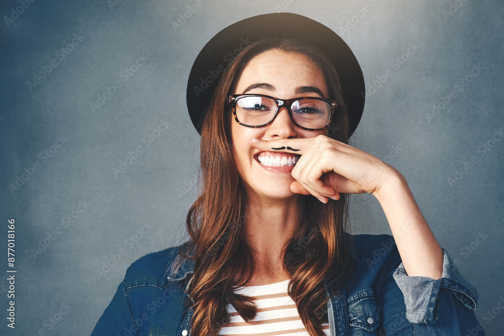 Sticker Excited woman, portrait and finger mustache, hat or goofy expression on a gray studio background. Female person, hipster or comedian with funny face impression, secret identity or fake hair.