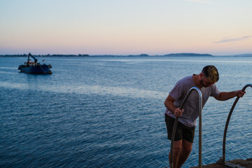 Fototapeta premium Man climbing stairs. back view on the sea shore. In the background the port, boat, pier.