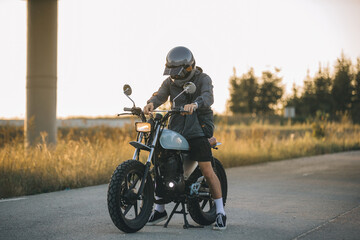 Obraz premium Biker man starts his motorcycle by turning the ignition key. Concept of riding a motorcycle at sunset.