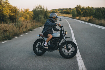 A young man in a helmet and goggles is enjoying his motorcycle on the road at sunset
