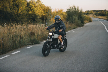 Fototapeta premium On the road, a biker drives his cafe racer motorcycle at sunset.
