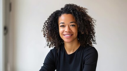 Fototapeta premium Young woman with curly hair smiling confidently in a black shirt. Bright and professional portrait for business or personal branding.