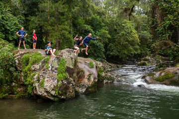 Dad with daughter jumping off rock into waterhole in lush forest