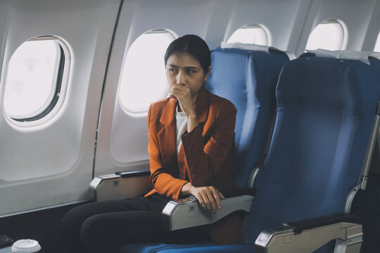 Stressed and serious young asian businesswoman remote working on the plane, suffering from headache and airsick during the flight.