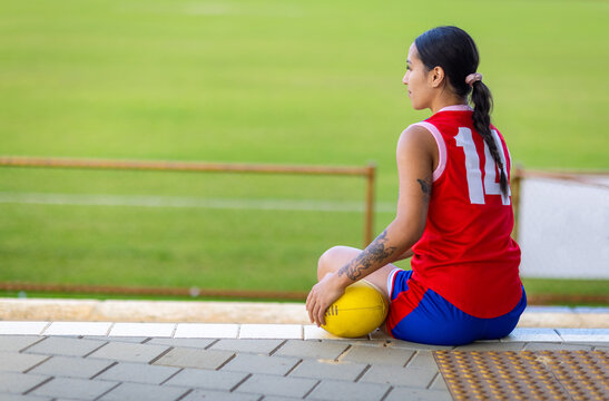 seen from behind one young lady football player seated on sidelines
