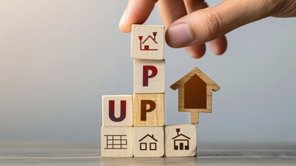 Hand stacking wooden blocks with house illustrations and the word 'UP', symbolizing real estate growth.