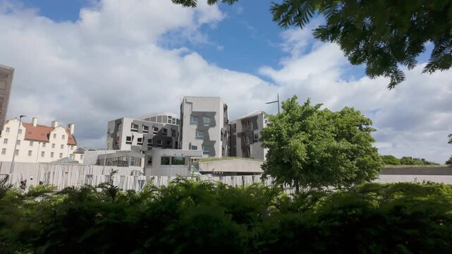 Camera rises to reveal side aspect of Holyrood Scottish Parliament in Edinburgh framed by trees on a sunny summer day 