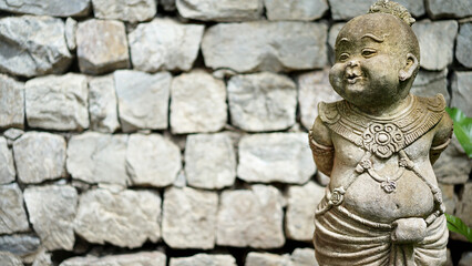Statue doll in traditional thai dress in front of stone wall. Black Magic baby. Decorate Stone doll.  Children statue in the garden.  Sculpture boy in Thai style. 