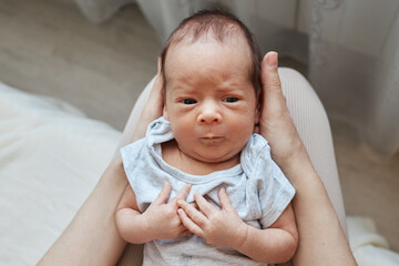 Unrecognizable mother holding newborn baby son wearing bodysuit woman spending time with her infant baby enjoying first days of motherhood