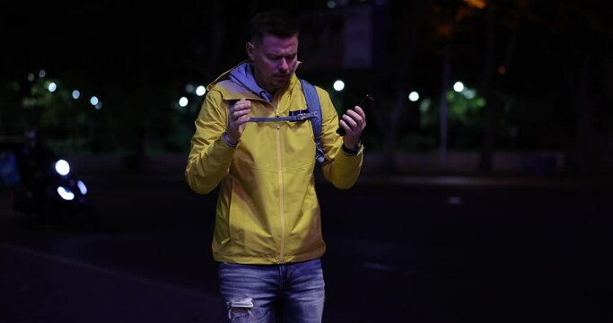 Male tourist uses navigation on smartphone to find train station. Desperate man got lost in unknown city standing on street at night slow motion