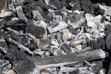 Charcoal pieces and ashes in a grill, showcasing the textures and contrasts typical of burnt wood and embers, illustrating a post-barbecue scene.