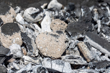 Charcoal pieces and ashes in a grill, showcasing the textures and contrasts typical of burnt wood and embers, illustrating a post-barbecue scene.
